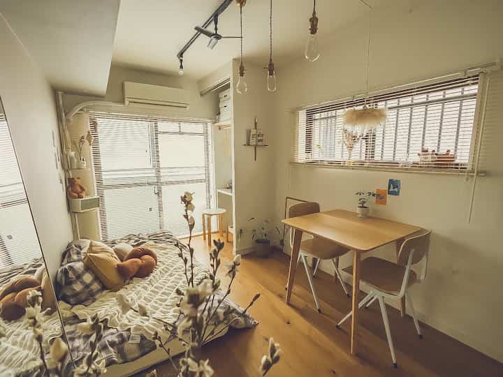 白と茶色のトーンのコンパクトな寝室、デスクとダイニングテーブルが配置された自然でシンプルモダンな印象的な空間