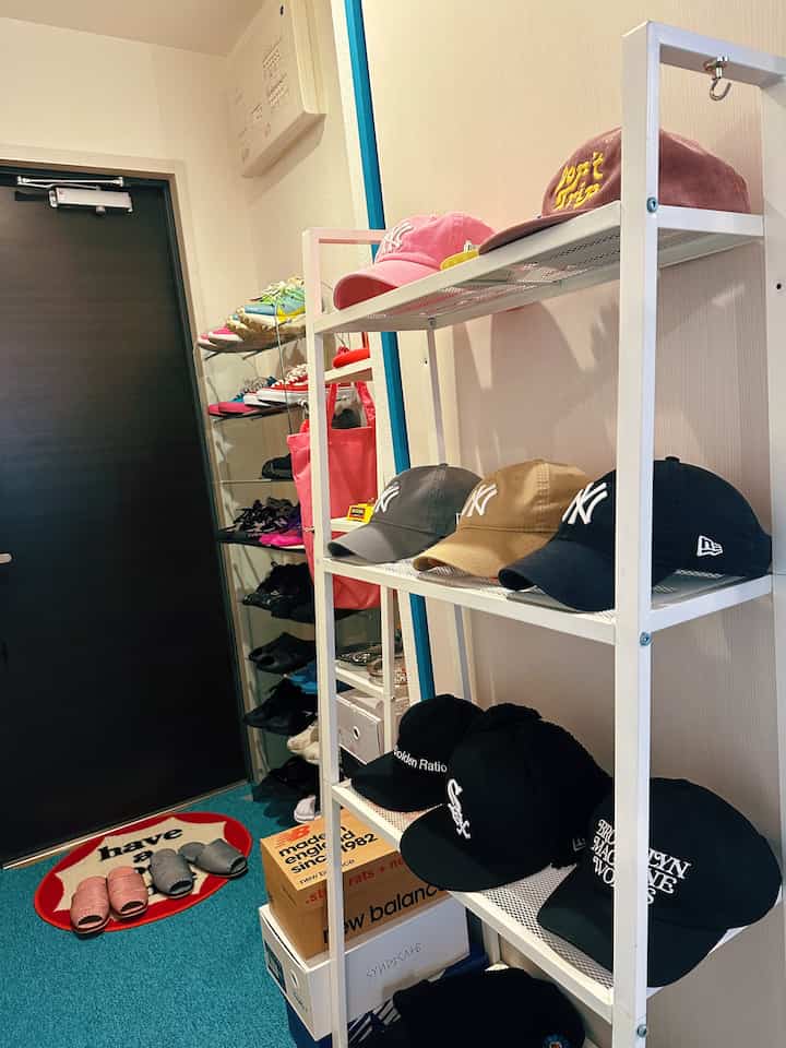 黒いドアと青いカーペットがある狭い玄関、整理された靴ラックと帽子棚が配置された印象的な空間