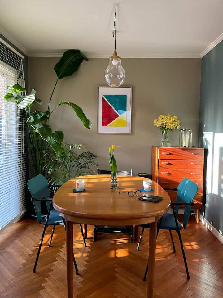 Dining room with green and beige toned walls featuring a wooden dining table and blue dining chairs, creating a natural atmosphere