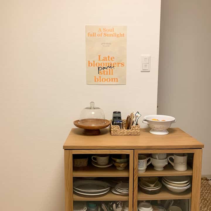 A simple kitchen space featuring a warm wood tone cabinet with kitchenware and a clean wall adorned with an orange text poster
