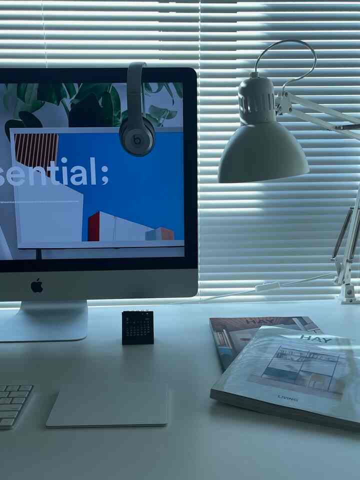 白を基調としたホームオフィスのワークスペース、ミニマルなデスクとモニター、照明、ヘッドホンが配置された雰囲気あるインテリア