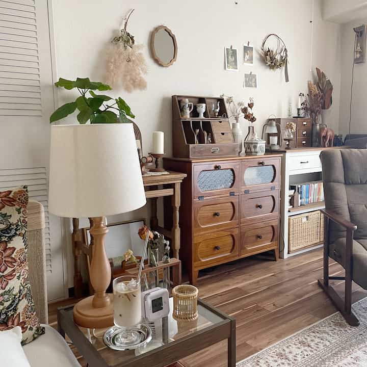 木目調とナチュラルな雰囲気のリビング、テーブルランプとアンティークチェストが配置された印象的な空間