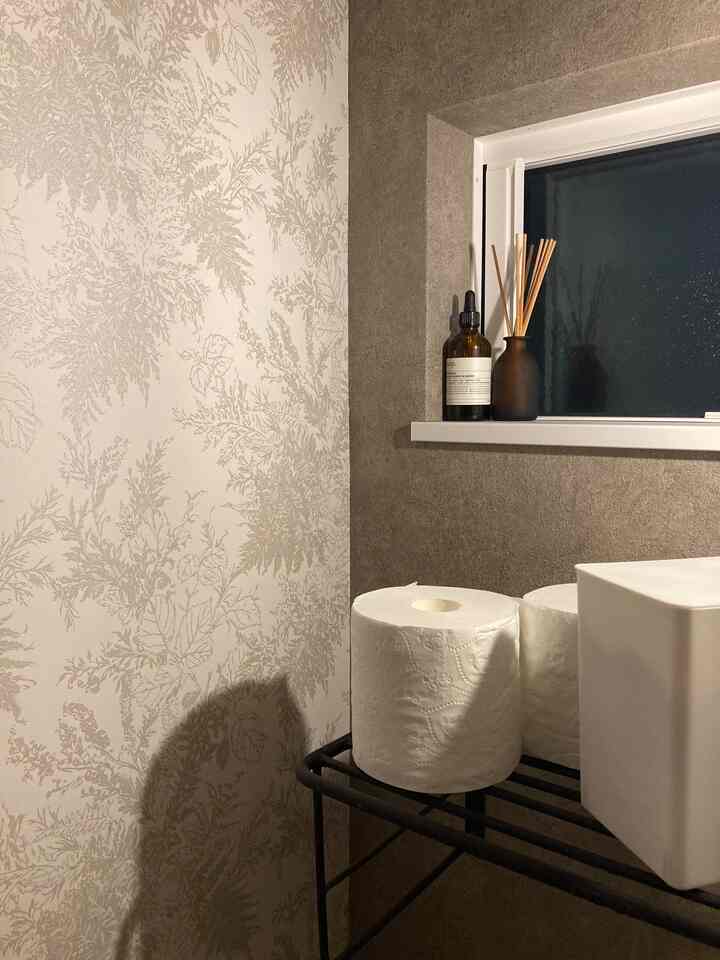 ベージュとブラウンの色調の狭いトイレ、植物柄の壁紙とディフューザーが配置された落ち着いた空間