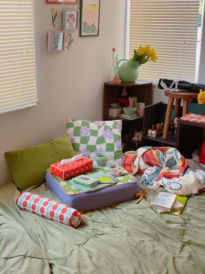 淡いグリーンのトーンの寝室、さまざまな柄のクッションとブランケットが置かれた暖かみのある空間