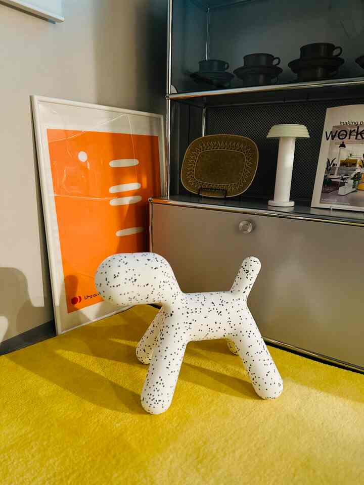 A modern space featuring a Dalmatian-patterned Puppy sculpture on a yellow rug and bright orange poster against a neutral wall