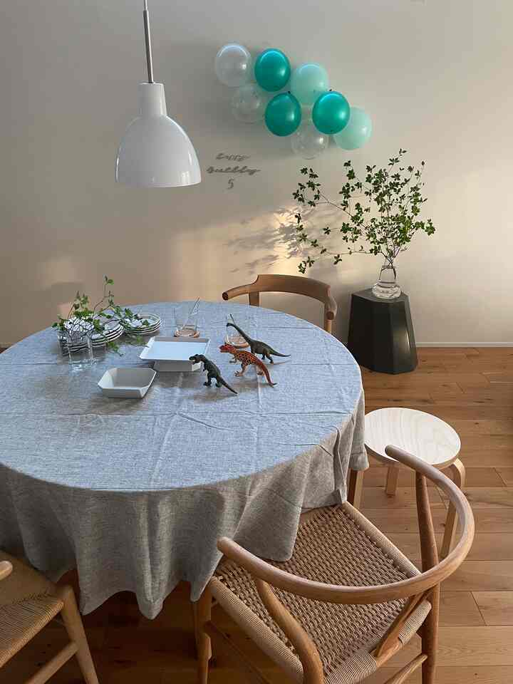 ナチュラルな木目調のシンプルなダイニング、柔らかなグレーのテーブルクロスをかけた丸い食卓と誕生日のバルーン装飾がある空間