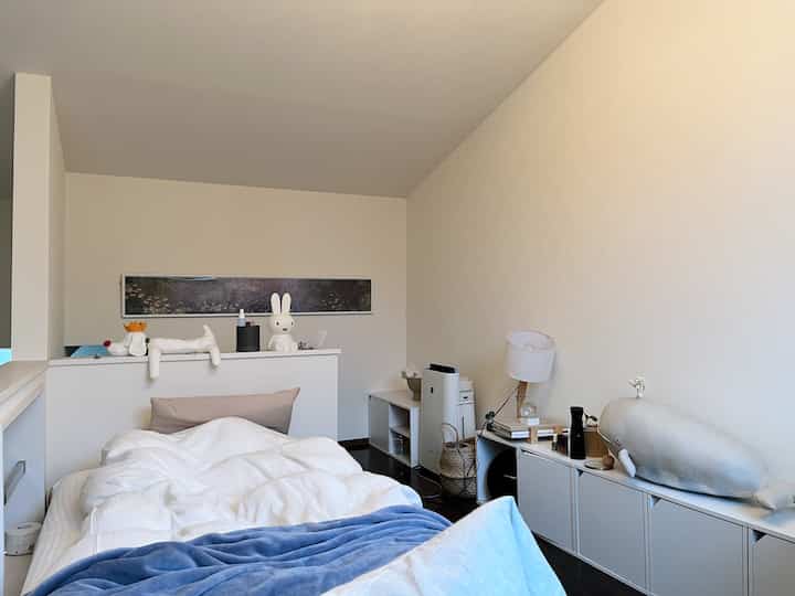 Cozy bedroom in white and beige tones featuring a white bed with cushions and a floor lamp on the right side.
