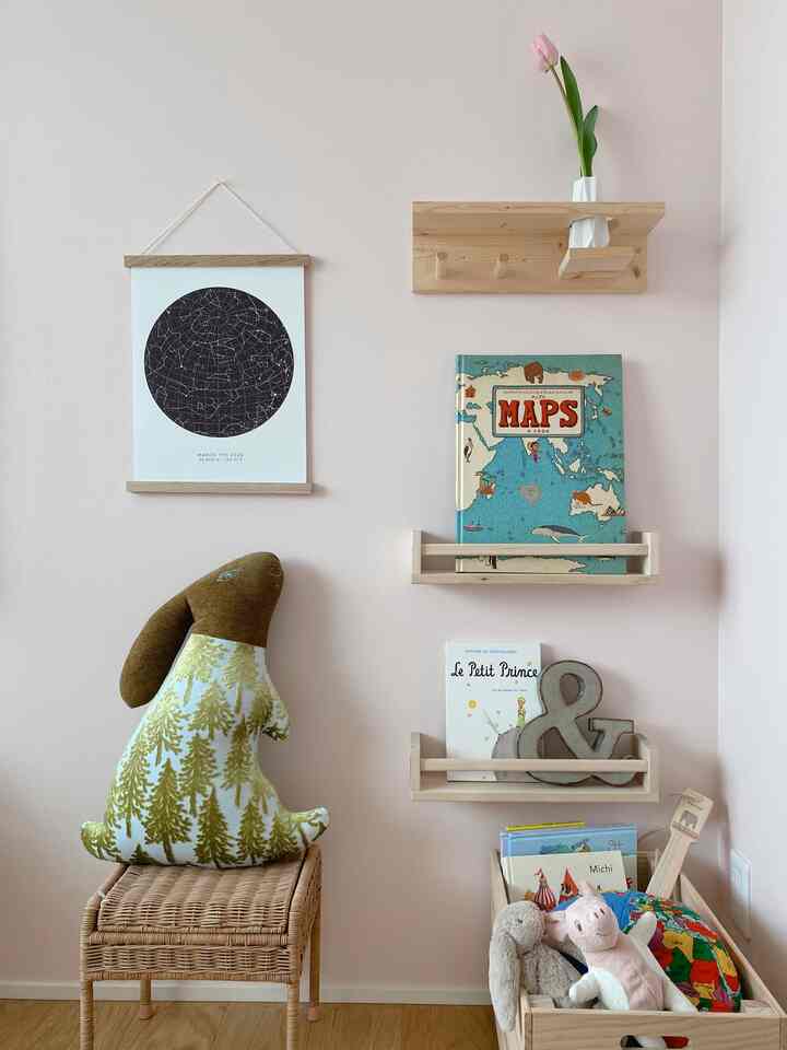柔らかなピンク色の壁と木目調の棚、子供向けの玩具収納が配置された印象的な子供部屋