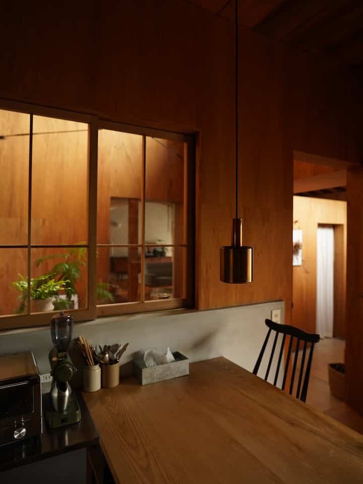 ダークブラウンの木目調が特徴のダイニング、木製のダイニングテーブルと黒いチェア、ペンダントライトが配置されたナチュラルな雰囲気のインテリア