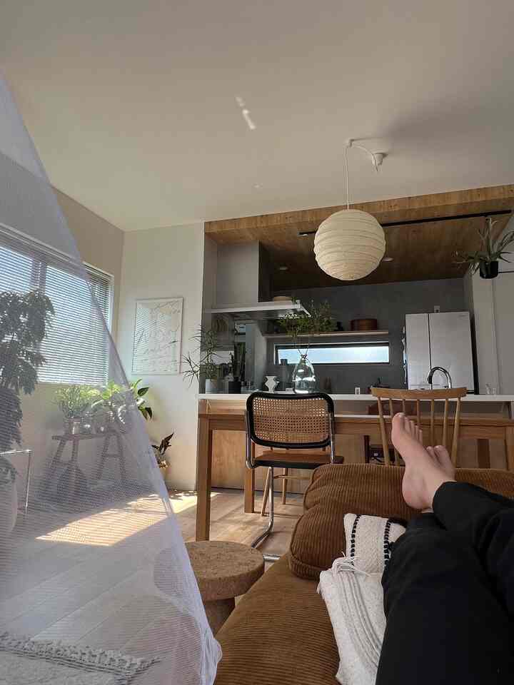 A natural-tone dining room featuring a beige armchair, wooden dining table, curtains, and plants creating a cozy atmosphere
