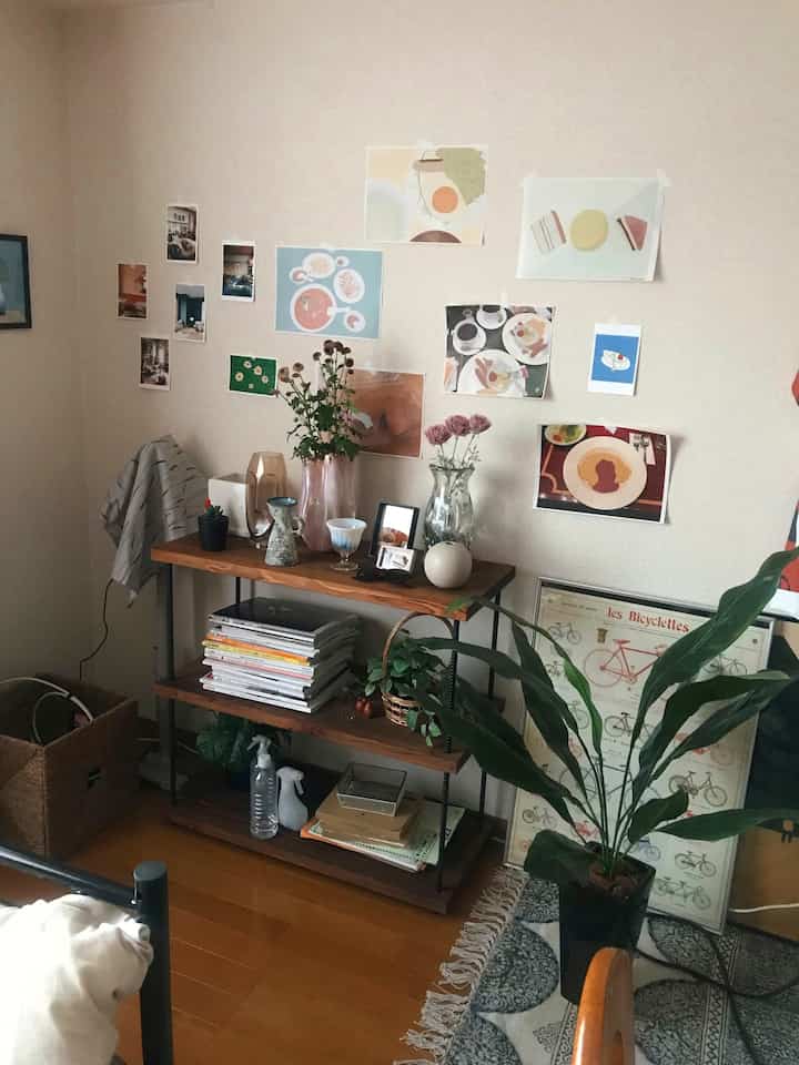 温かみのあるナチュラルカラーのリビング、木製の棚と植物、多様なアートが壁に配置された雰囲気あるインテリア