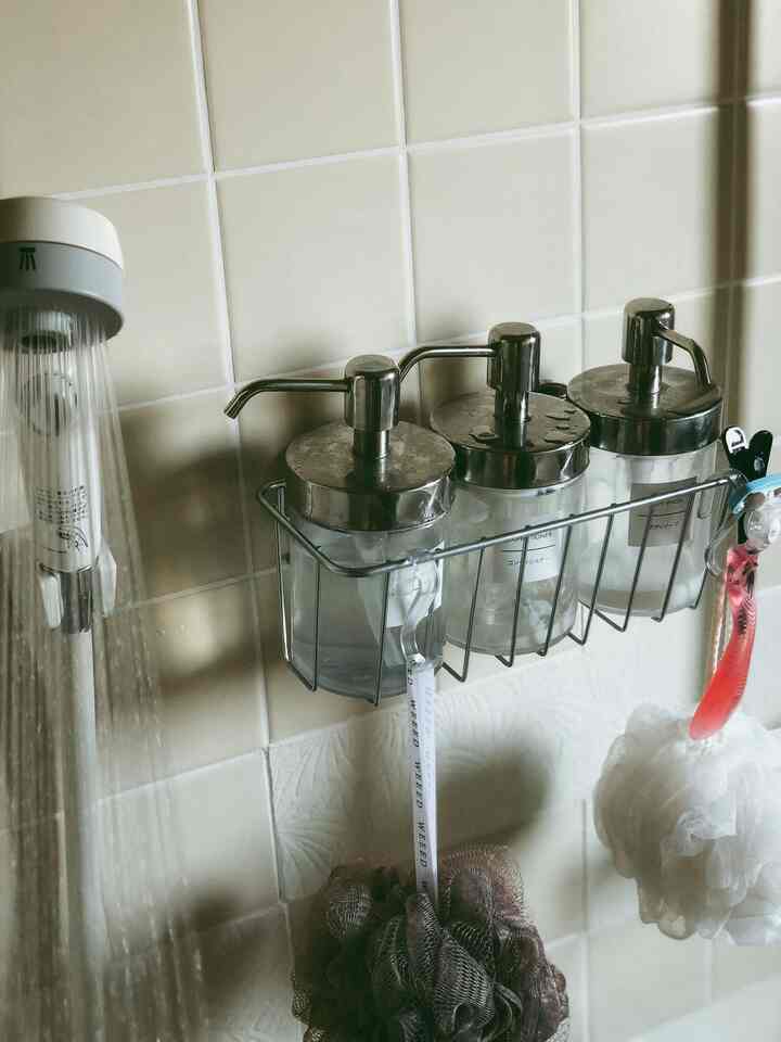 ベージュのタイル壁にステンレス製ポンプボトルと白いバススポンジが配置された、清潔感のある整理されたバスルーム