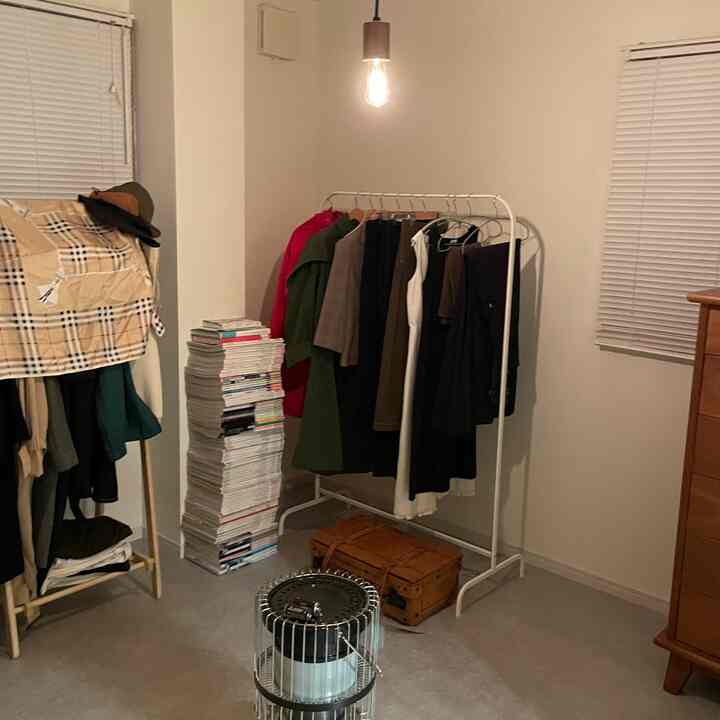 White-toned small closet space featuring two clothing racks, retro brown dresser, and a vintage heater centrally placed