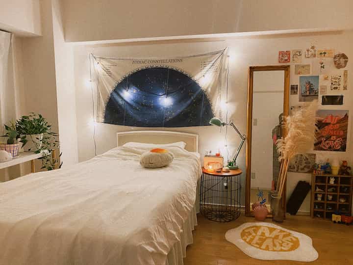 A white and wood tone bedroom featuring a zodiac tapestry, string lights, and a table lamp on the side table, creating a calm resting space