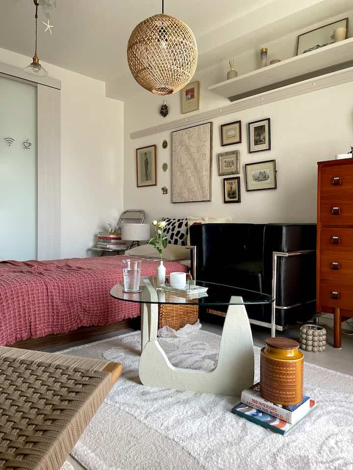 自然なブラウンとホワイトのトーンのリビング、黒のソファとラタン製ペンダントライトが配置された雰囲気のあるインテリア