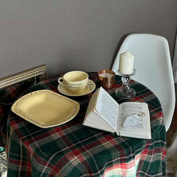 クリーム色の食器とガラスのキャンドルスタンドが配置されたチェック柄のテーブルと白い椅子がある雰囲気のあるおうちカフェ