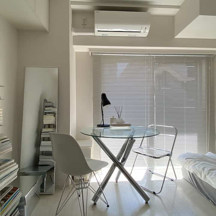 White and silver toned studio apartment dining area featuring a glass dining table with chairs, showcasing a modern minimalist style