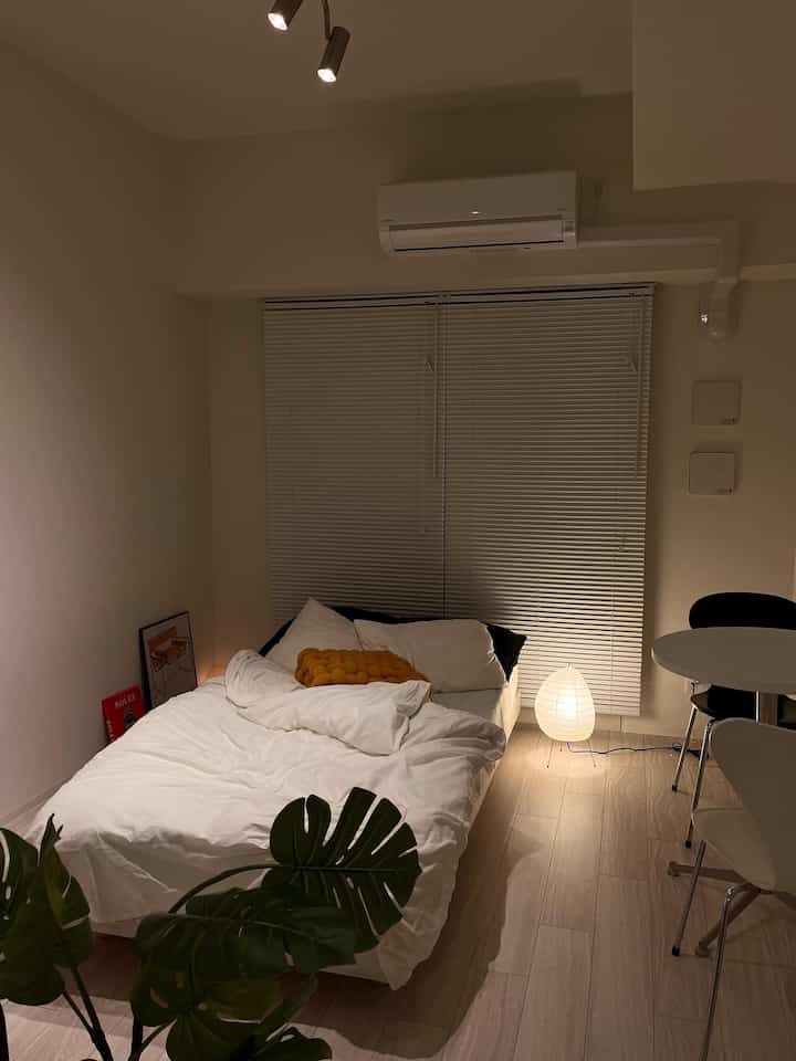 ホワイトとナチュラルトーンの小さな寝室、イサムノグチAkariフロアランプとモンステラ植物が配置されたモダンな一人暮らしの空間