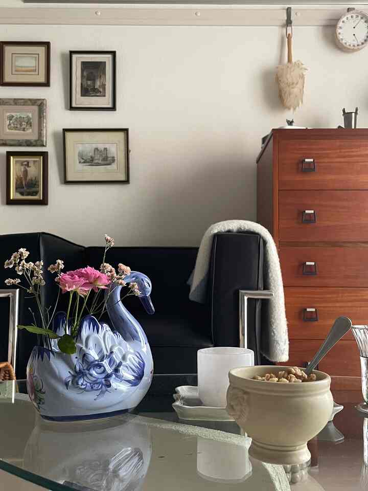 白い壁とナチュラルウッドのキャビネットがあるリビング、黒いソファとガラステーブルにピンクの花瓶が置かれた雰囲気のある空間