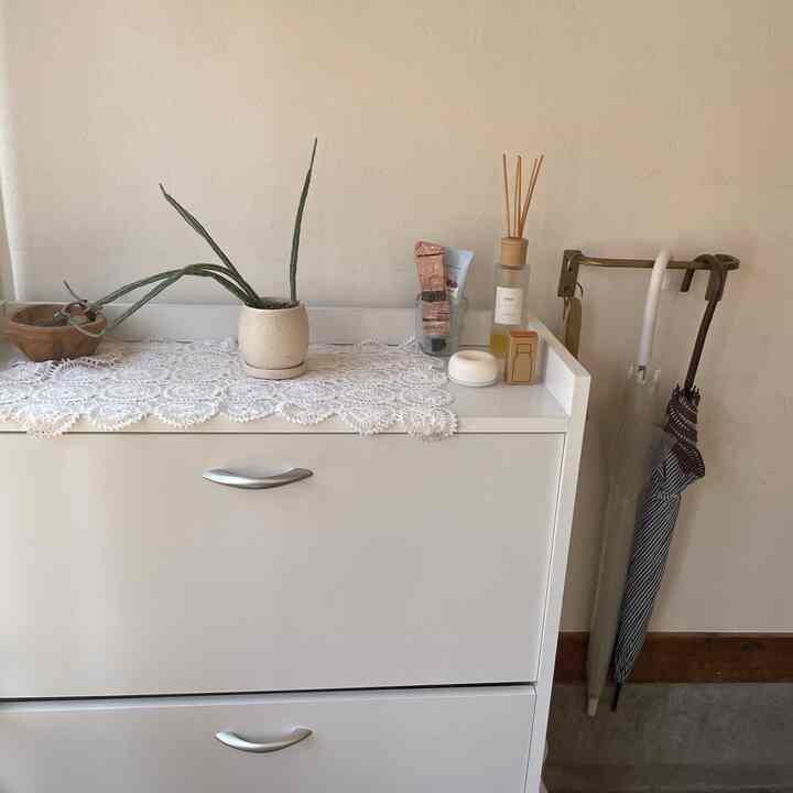 ベージュの壁と白いシューズラックがある玄関、アロマストーンと装飾品が配置された清潔で温かみのある雰囲気のインテリア