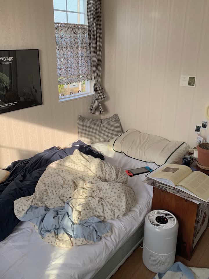 ベージュの壁紙とナチュラルな雰囲気の寝室、清潔感のある白い寝具と木製デスクが配置された落ち着いた空間