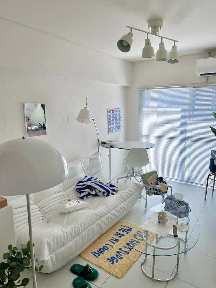 Bright white and natural toned living room featuring a white sofa and glass coffee table, creating a simple and compact atmosphere