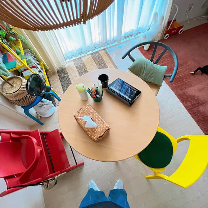 ナチュラルな木目調のベランダ隣接空間、丸いダイニングテーブルとカラフルな椅子、赤ちゃん用家具が調和した印象的なインテリア