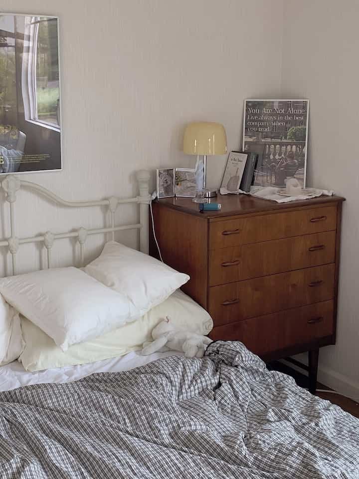 アイボリー色の壁とナチュラルな木製家具が配置された寝室、整ったベッドと黄色のテーブルランプがある雰囲気の良い空間