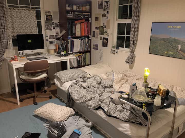 Natural color and wood tone compact bedroom and home office space featuring bookshelf, bed, and desk in a cozy room