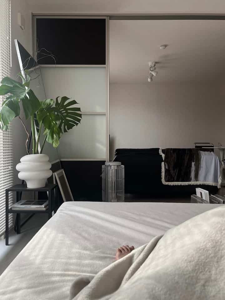 白と黒のモノトーンの寝室、ベッドとナイトテーブル、ソファ、植物が配置されたモダンで落ち着いた雰囲気のインテリア
