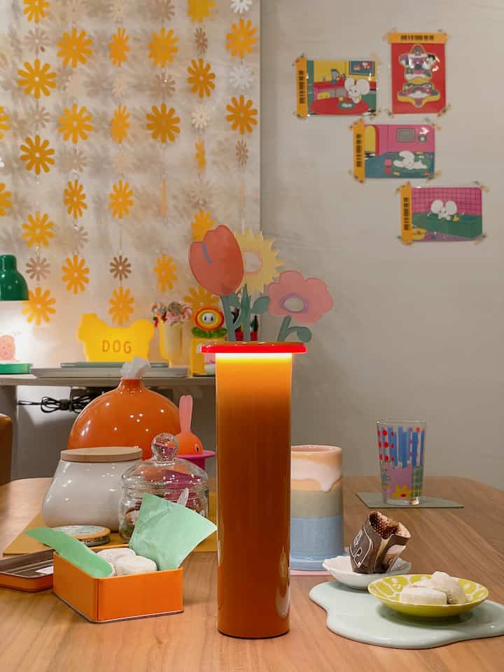 オレンジとナチュラルカラーが調和したミッドセンチュリーモダンのダイニングルーム、中央に花の装飾があるテーブルランプが配置された印象的な空間