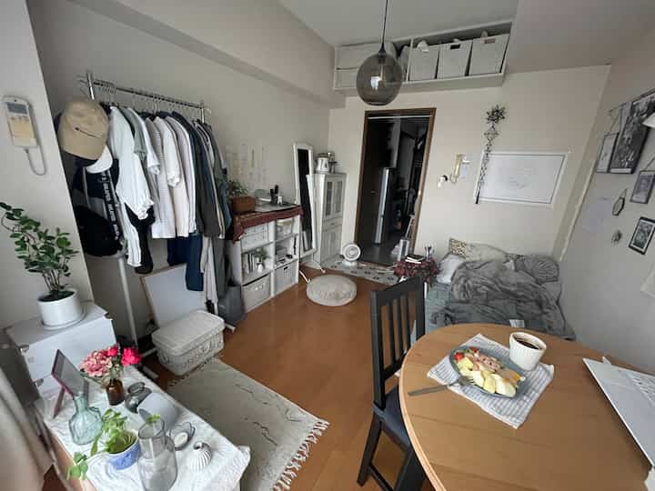 ナチュラルな色調と白い壁の6畳の狭い部屋、マルチソファと丸いダイニングテーブルが置かれた居心地の良い一人暮らしの空間