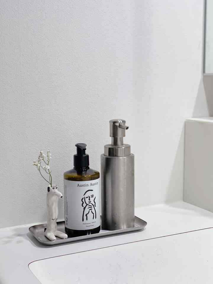 White and gray toned bathroom sink area with a tray holding two types of hand soaps and a small vase in a minimalist setting