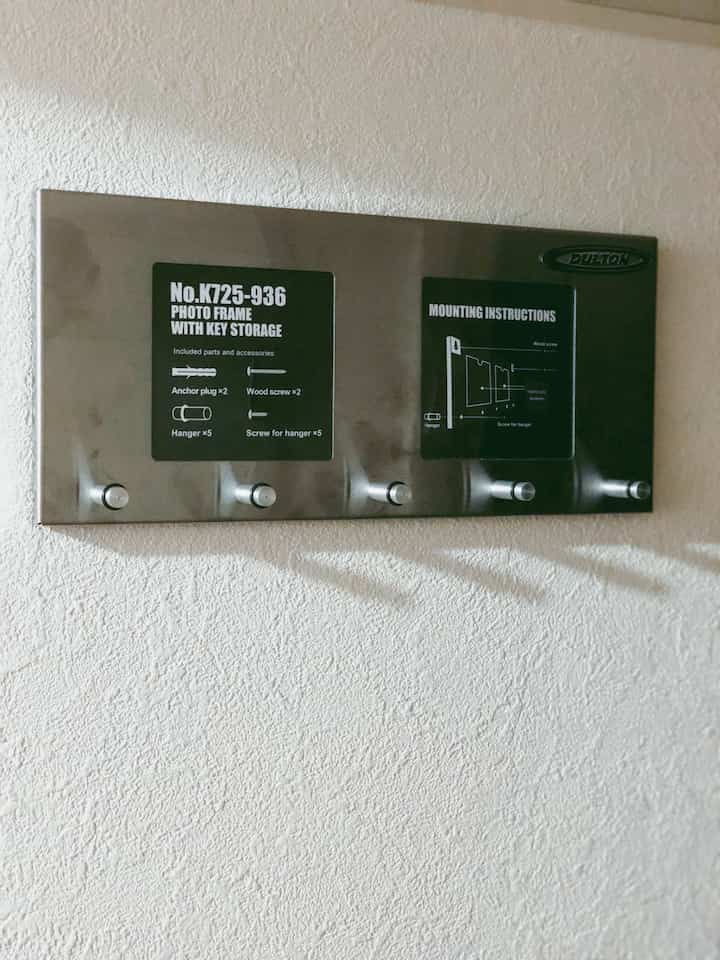 白い壁にステンレス製の鍵収納付きフォトフレームが配置されたシンプルな玄関のインテリア