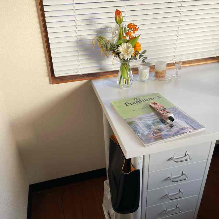 白と茶色のトーンが美しい狭い部屋、白いデスクと引き出しが配置され、花瓶とキャンドルが置かれた雰囲気のあるワークスペース