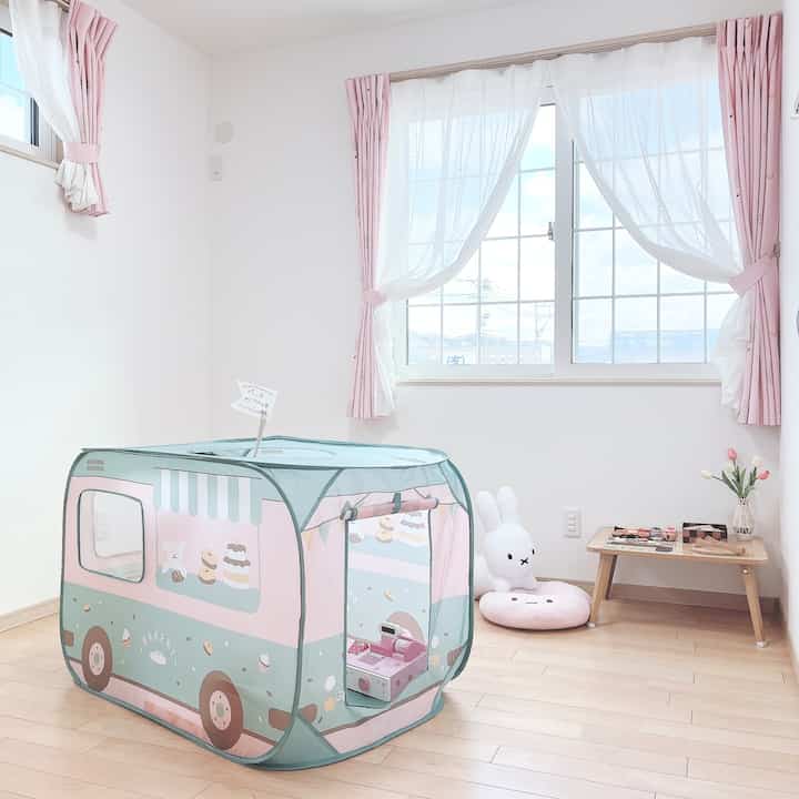白い壁と木目調の床の子供部屋、ピンクのカーテンとキッズプレイテントが配置された明るい空間