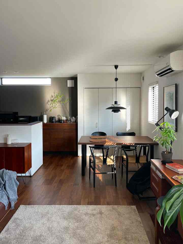 ダークブラウンの床と木製家具が配された白い壁のキッチン兼ダイニングルーム、自然光が差し込むナチュラルモダンな空間