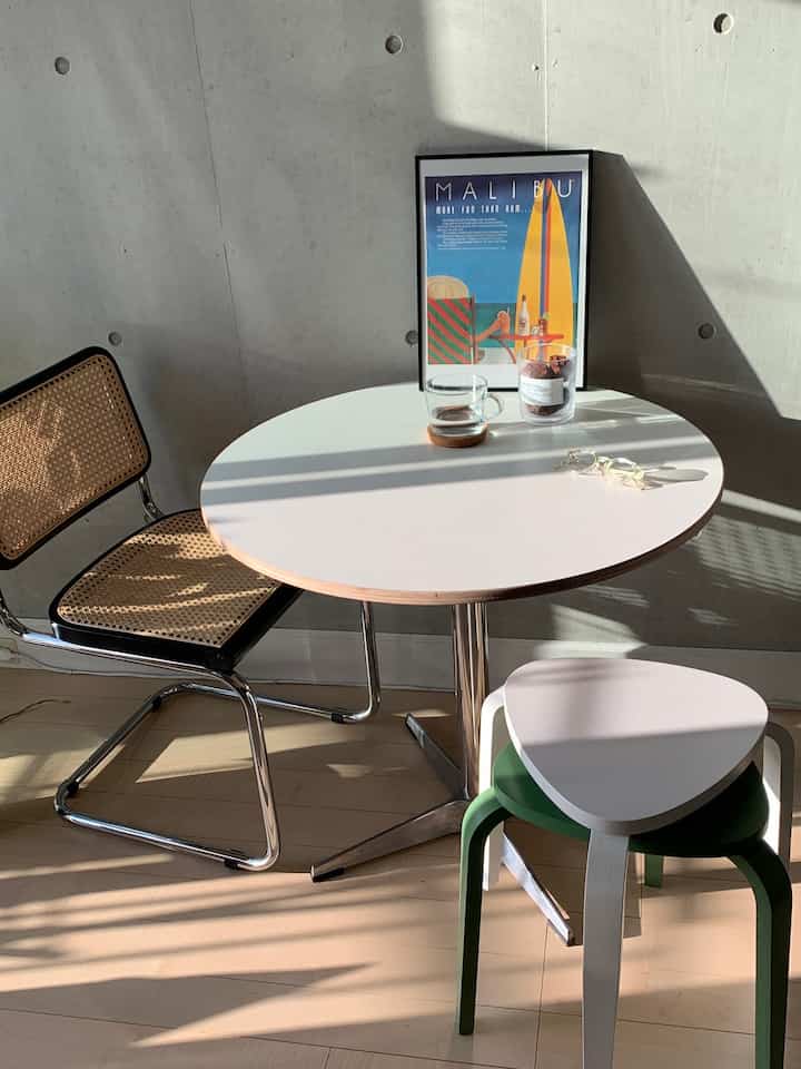 Bright white round dining table with natural wood flooring in a two-person household space, featuring warm sunlight and minimal atmosphere