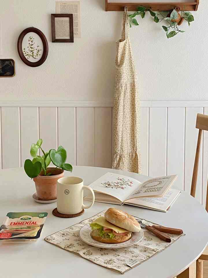 白い壁とテーブル、植物とサンドイッチが置かれたナチュラルな雰囲気のダイニングインテリア