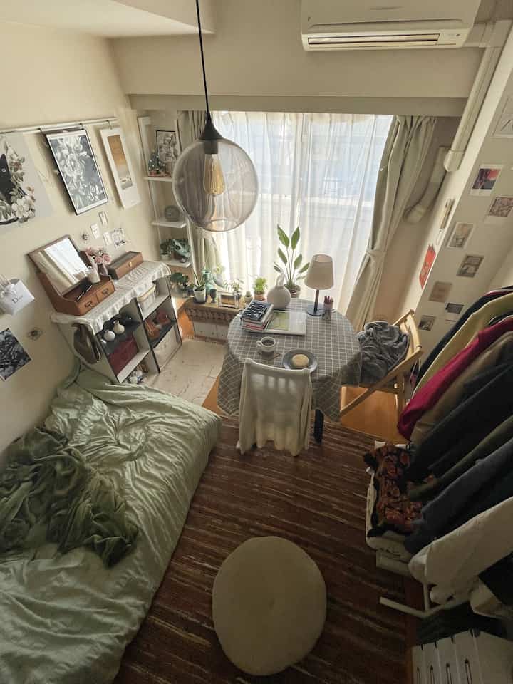 ベージュ調のワンルーム寝室、窓辺にテーブルと植物が配置された雰囲気のあるナチュラルインテリア