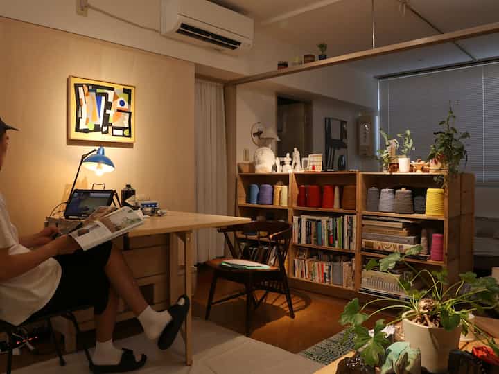 Warm natural-tone single household living space featuring a desk, chair, colorful yarn shelves, books, and plants creating a cozy atmosphere