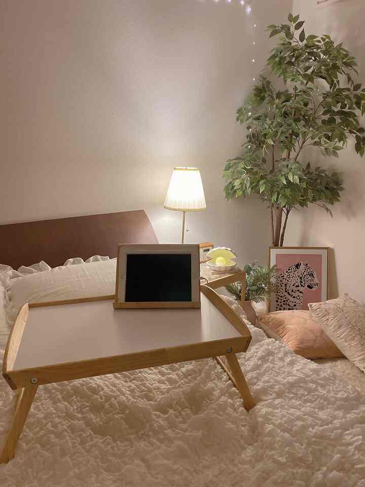 White and brown bedroom featuring a central bed with wooden tray, green plant, and pink leopard art poster on the right, creating a cozy atmosphere
