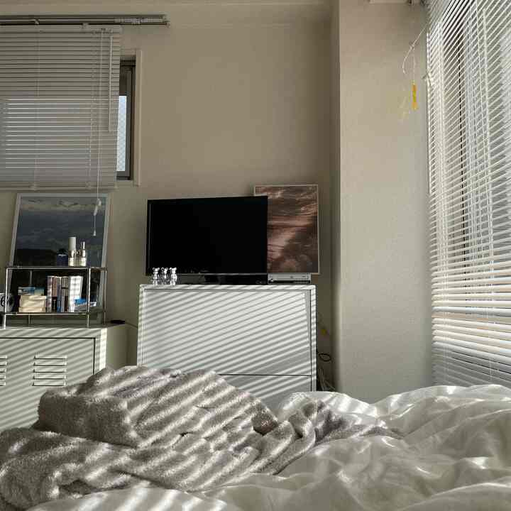 白の色調の寝室、白いブラインドと収納家具が配置された落ち着いた雰囲気の空間