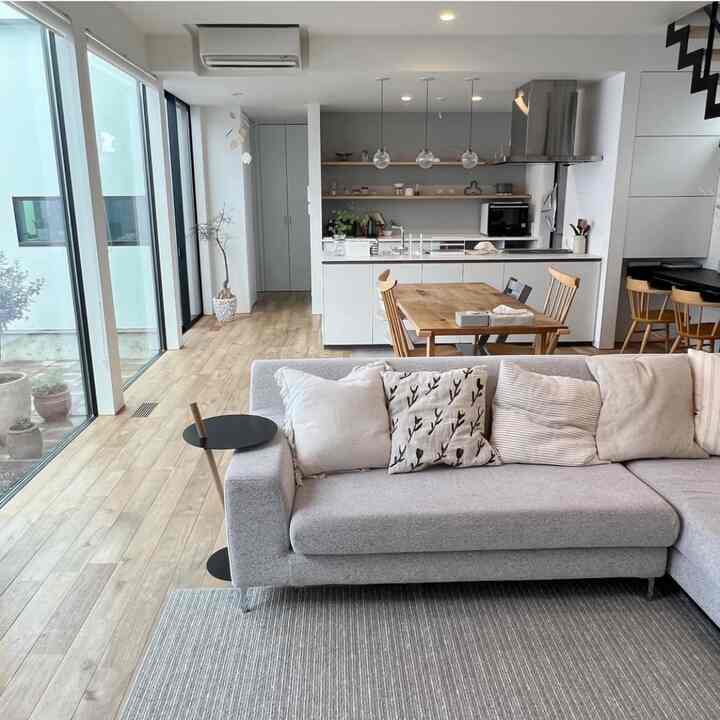Bright natural color tone long living room and kitchen space featuring a gray sofa and wooden dining table in Nordic style interior