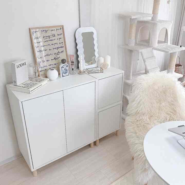White and natural color living room featuring white storage cabinet and cat tower in a minimalistic interior space