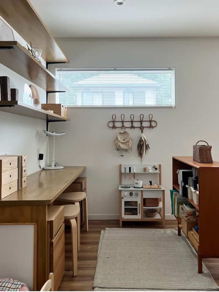 Natural toned kids' room featuring wooden desk and stools with a children's play kitchen, creating a cozy atmosphere