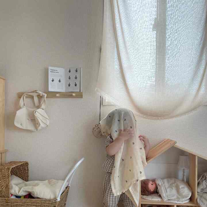 ナチュラルな色調の子供部屋、木目調のおもちゃ収納とベージュのカーテンが配置された雰囲気のある空間