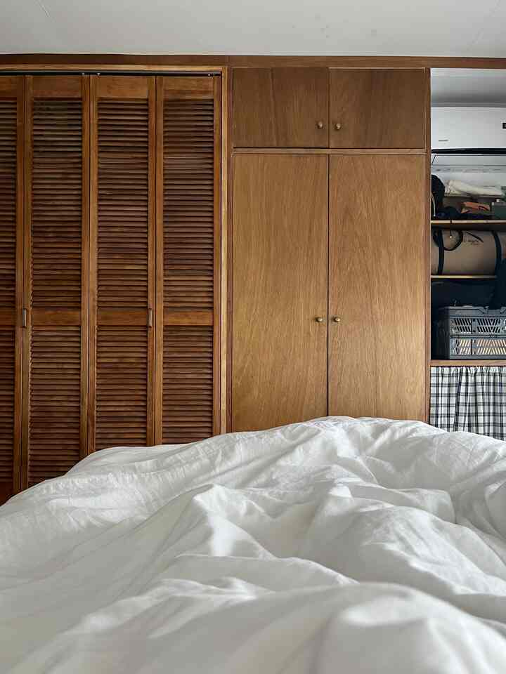 木目調と白い寝具が調和した寝室、大きな木製クローゼットが配置された落ち着いた空間