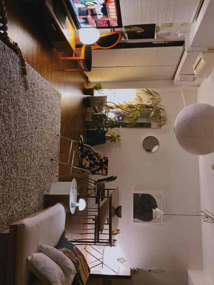 White and brown toned living room featuring sofa, dining table, plants, and pendant lighting with natural modern ambiance