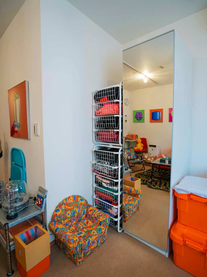 白とベージュの色調の子供部屋、カラフルな子供用椅子と壁美術品、大きな全身鏡が配置された雰囲気のある空間